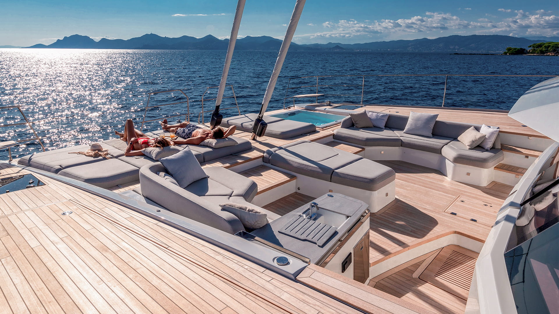 Guests lounging on the foredeck sunpads of the Fountaine Pajot Thira 80 with a coastal mountain view